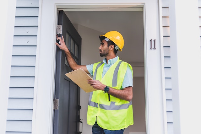 a property inspector in a yellow vest and hard hat looking at the home's doorway
